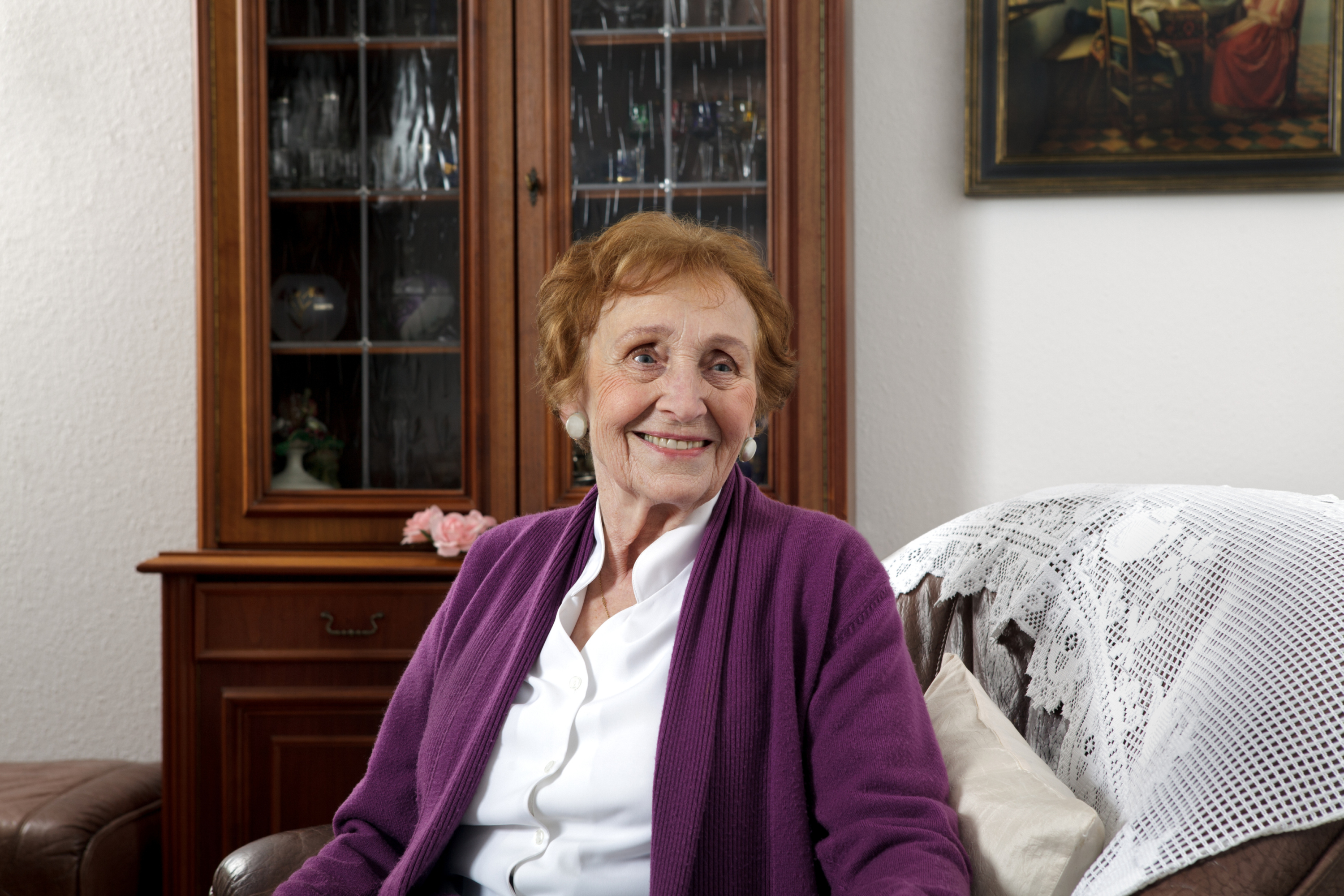 Sozialstationen und Ambulante Pflege Eine alte Dame sitzt lächelnd auf dem Sofa in ihrem Wohnzimmer